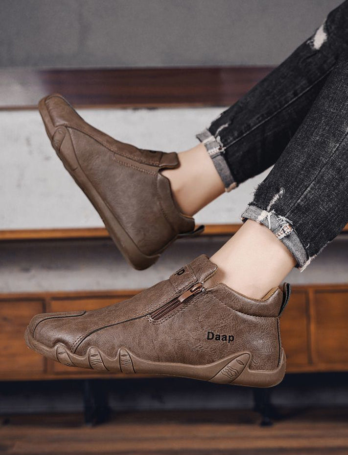 Brown shoes with a brand logo worn by a person on a wooden floor.