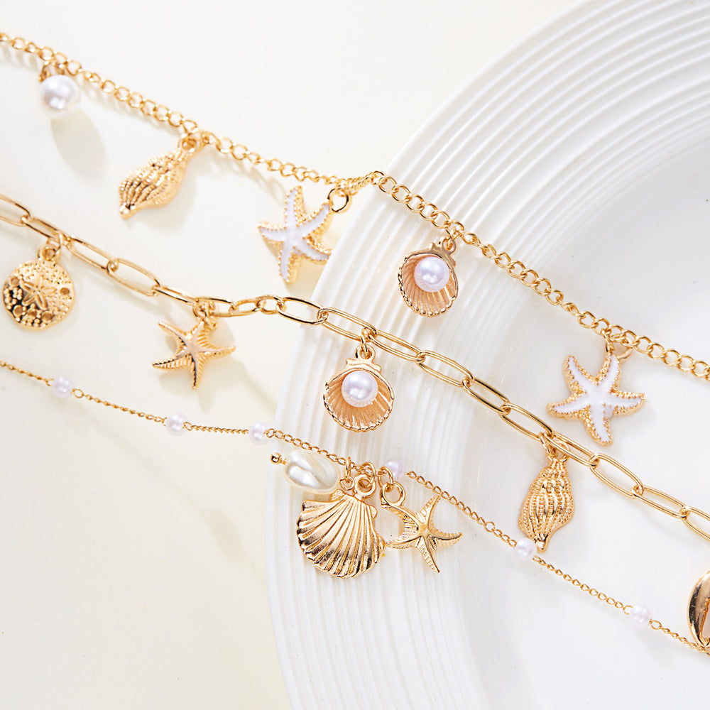 Gold anklets with shell and starfish charms on a white seashell background