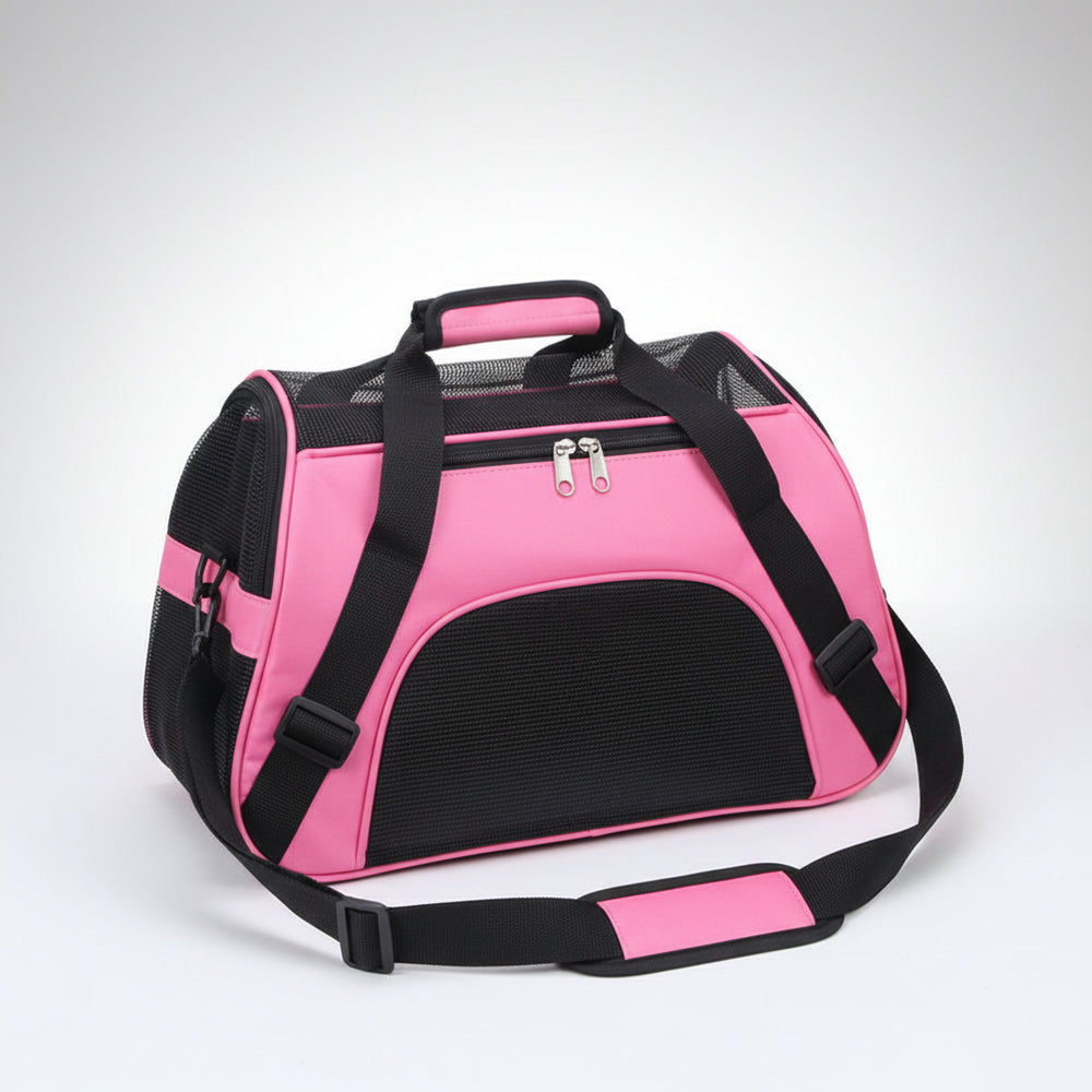 Pink pet carrier with black straps on a brown floor.