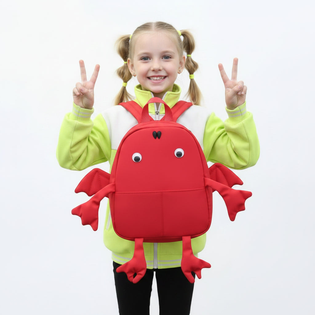 Child wearing a red crab-shaped backpack with a neutral background