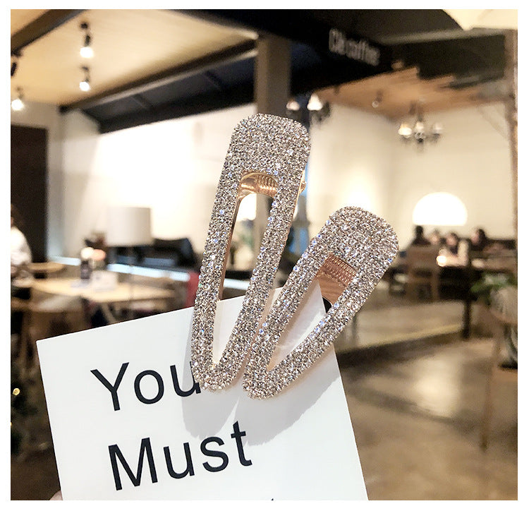Silver hair clips with rhinestones on a white card with 'You Must' text, blurred restaurant background