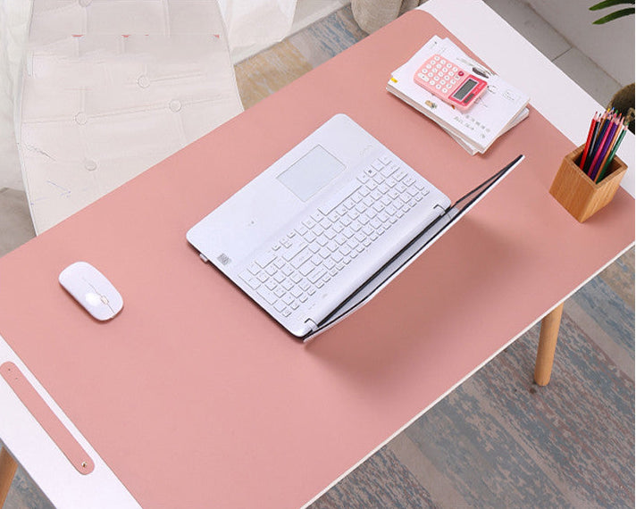 Pink desk with laptop, mouse, and stationery on a wooden floor.
