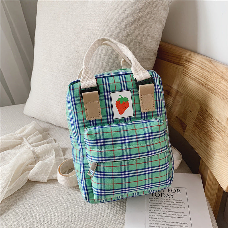 Green plaid bag with a strawberry patch design on a bed