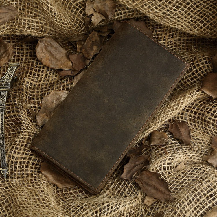 A dark brown leather journal or notebook with visible stitching, placed diagonally on a textured burlap fabric with scattered dried leaves.