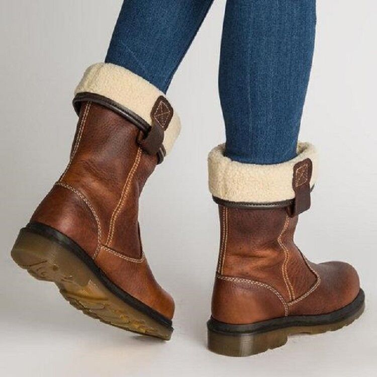 Brown ankle boots with white fur lining worn with blue jeans on a light gray background
