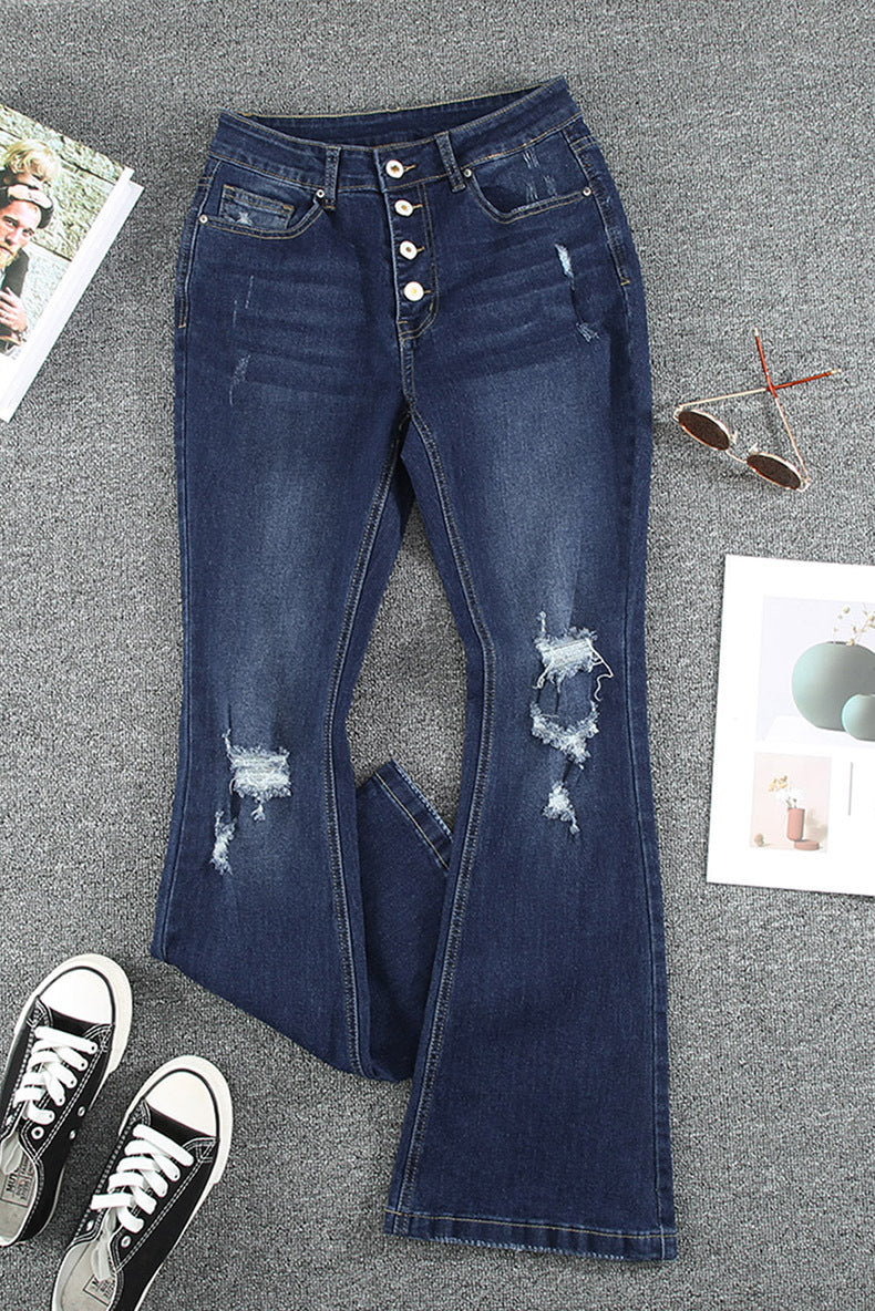 Distressed blue jeans on a gray surface with sneakers and sunglasses.