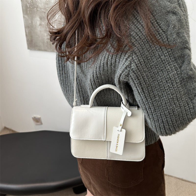 Person wearing a gray sweater holding a white handbag with a visible brand tag.