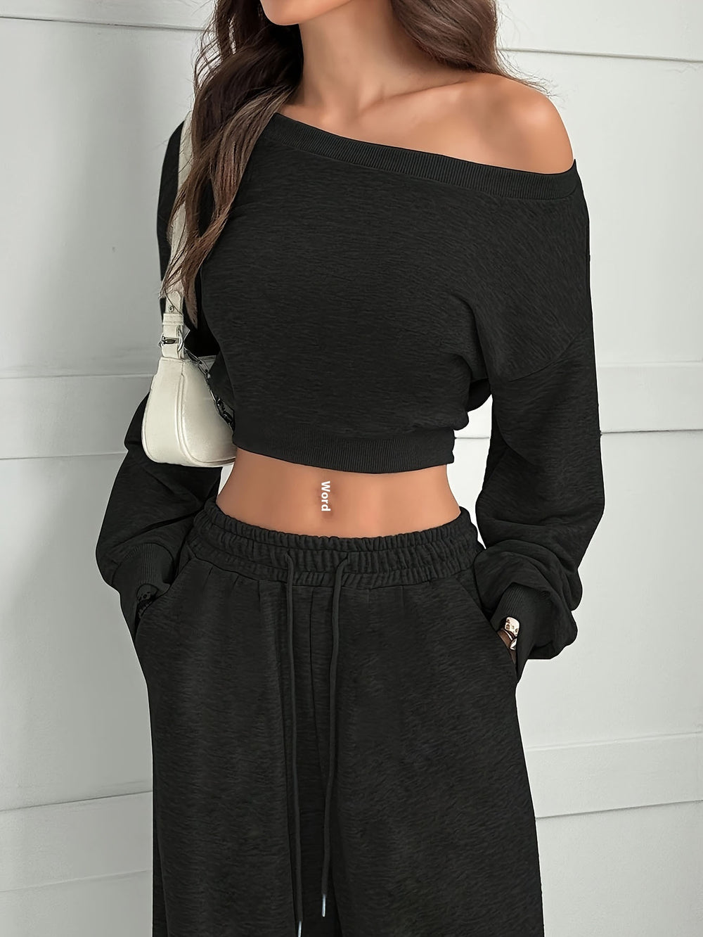 Person wearing a black off-shoulder top and black pants against a white wall.