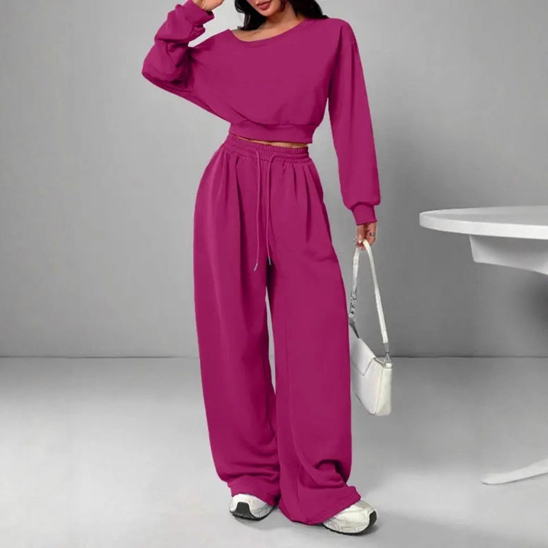 Person wearing a magenta outfit with wide-leg pants and a matching top, holding a white handbag.