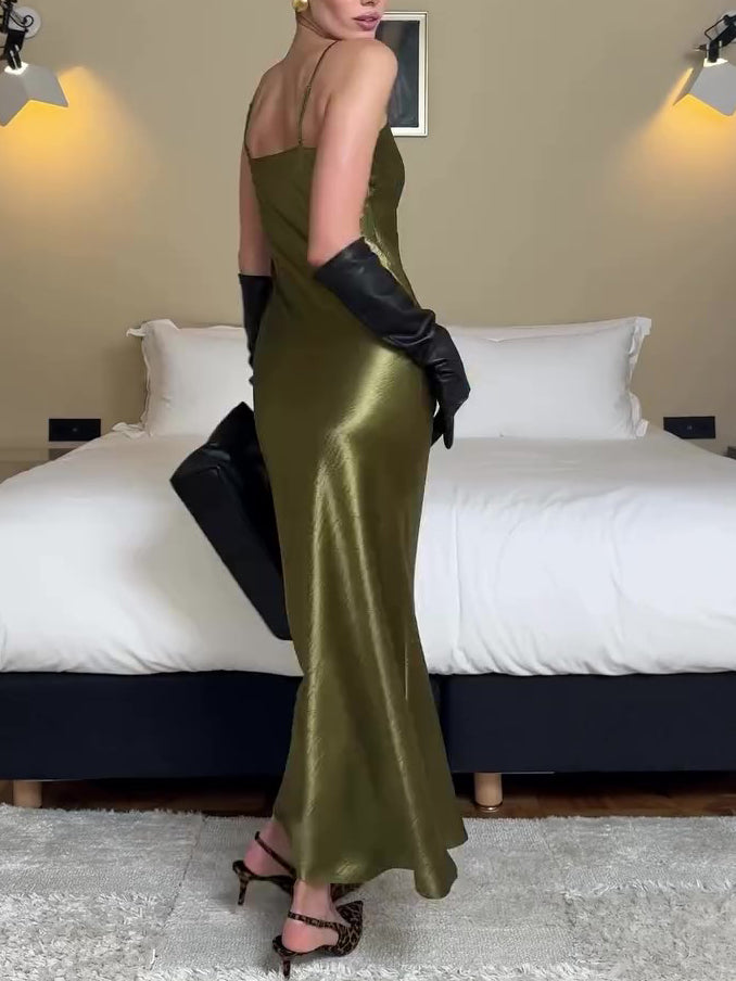 Woman in a green satin dress and black gloves standing in a bedroom.