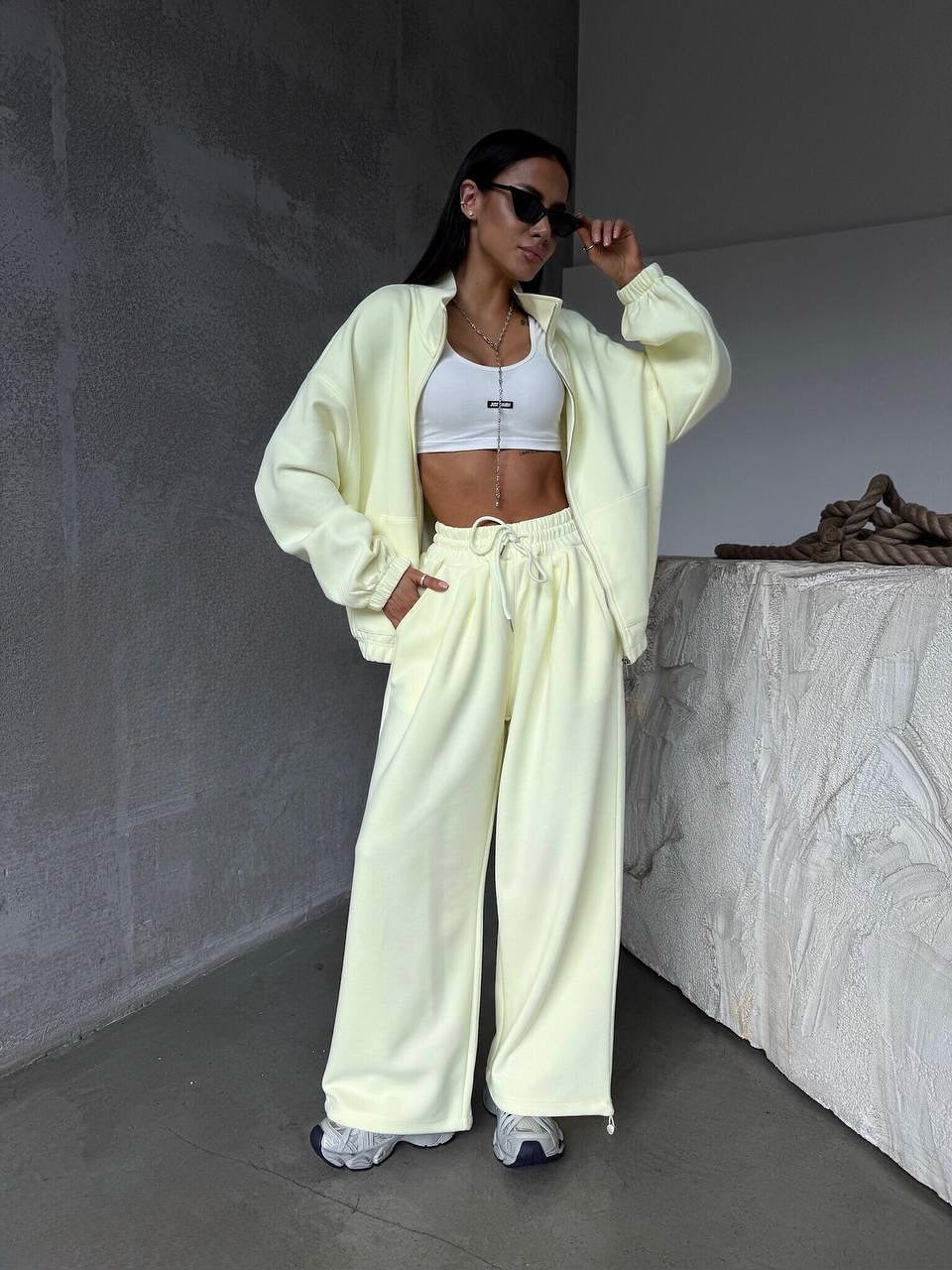 Person wearing a light yellow tracksuit with a white top in a minimalistic setting.