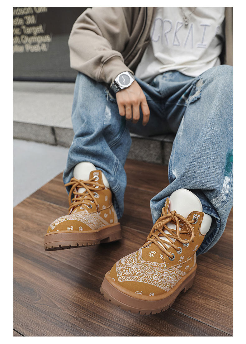 A person seated on concrete steps wearing tan bandana-print lace-up boots with white socks and light blue jeans.