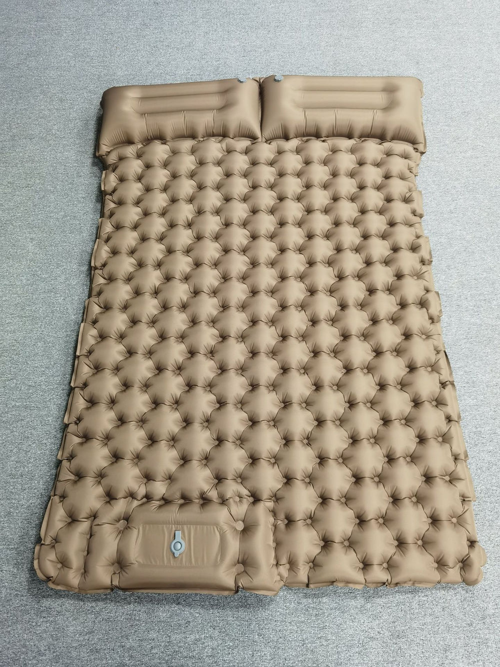 A tan inflatable sleeping pad with a quilted bubble pattern and two integrated headrests, laid flat on a gray textured surface.
