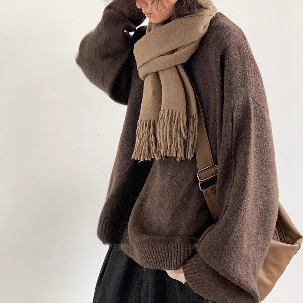 Person wearing a brown sweater and scarf with a matching bag on a white background