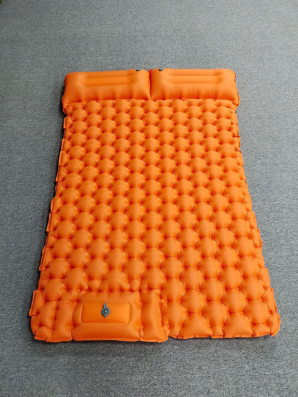 An orange inflatable camping sleeping pad with a honeycomb bubble design, laid flat on a gray textured surface.