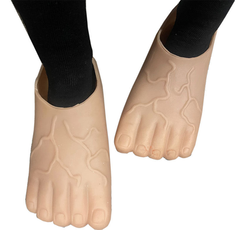 A pair of beige, foot-shaped shoe covers with textured, raised patterns resembling skin creases, shown worn on feet with black socks against a white background.