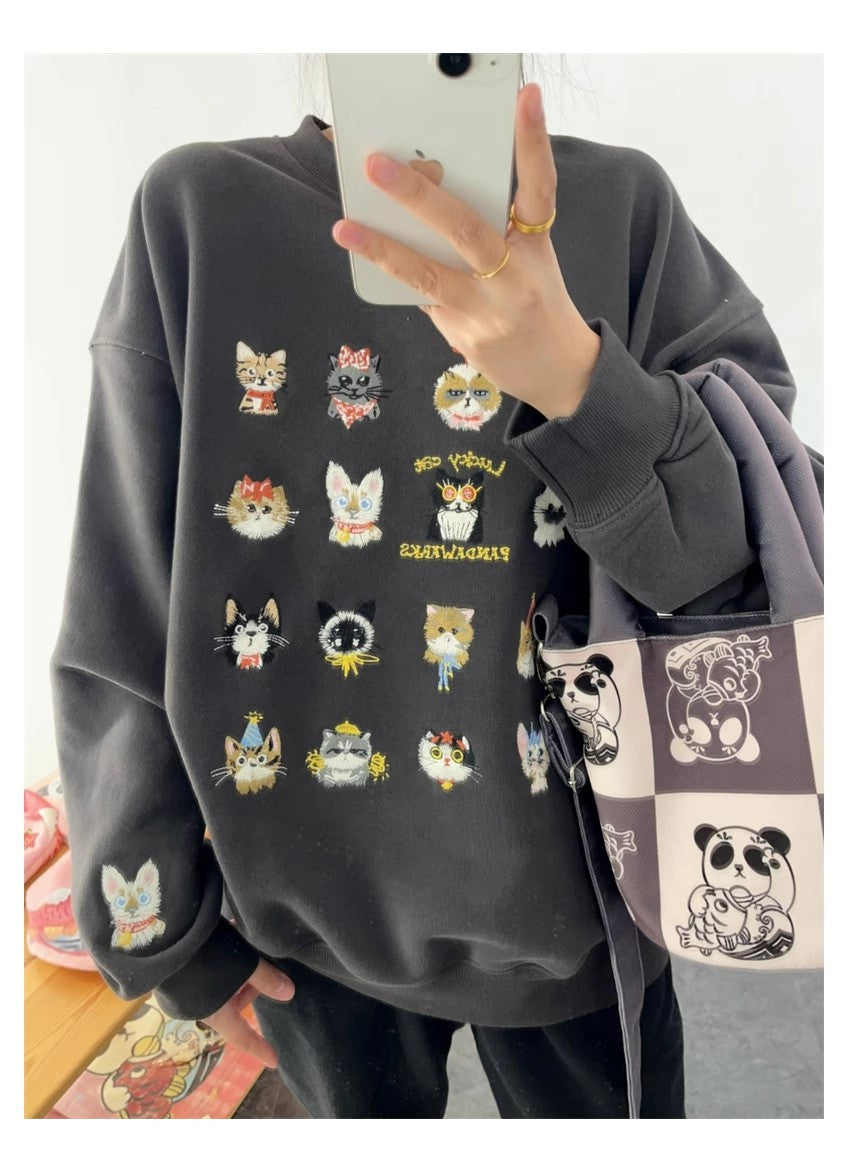 Person wearing a dark gray sweatshirt with cat illustrations, holding a phone.