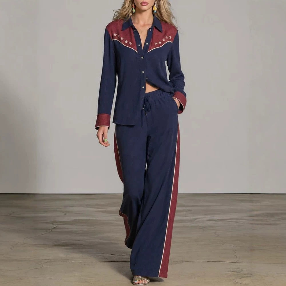 A woman models a matching two-piece western-style lounge set consisting of a long-sleeve button-up shirt and wide-leg pants. The set is navy blue with burgundy panels on the chest and cuffs, accented with white western embroidery on the shirt collar and shoulders, and white side stripes on the pants.