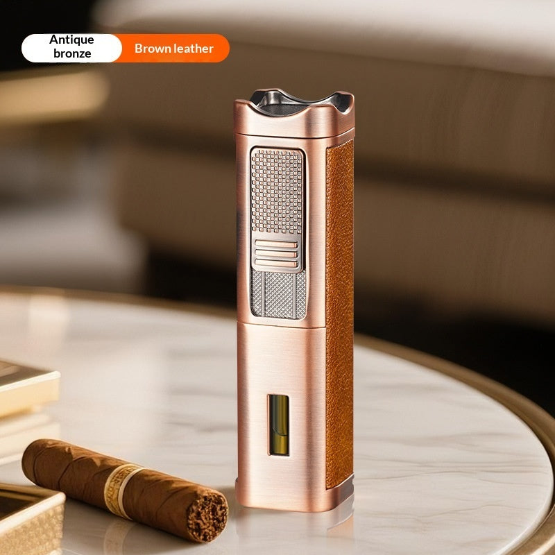 A metallic bronze and brown leather cigar torch lighter stands on a round marble table next to a cigar, with a blurred indoor background. An overlay at the top left reads 'Antique bronze Brown leather'.