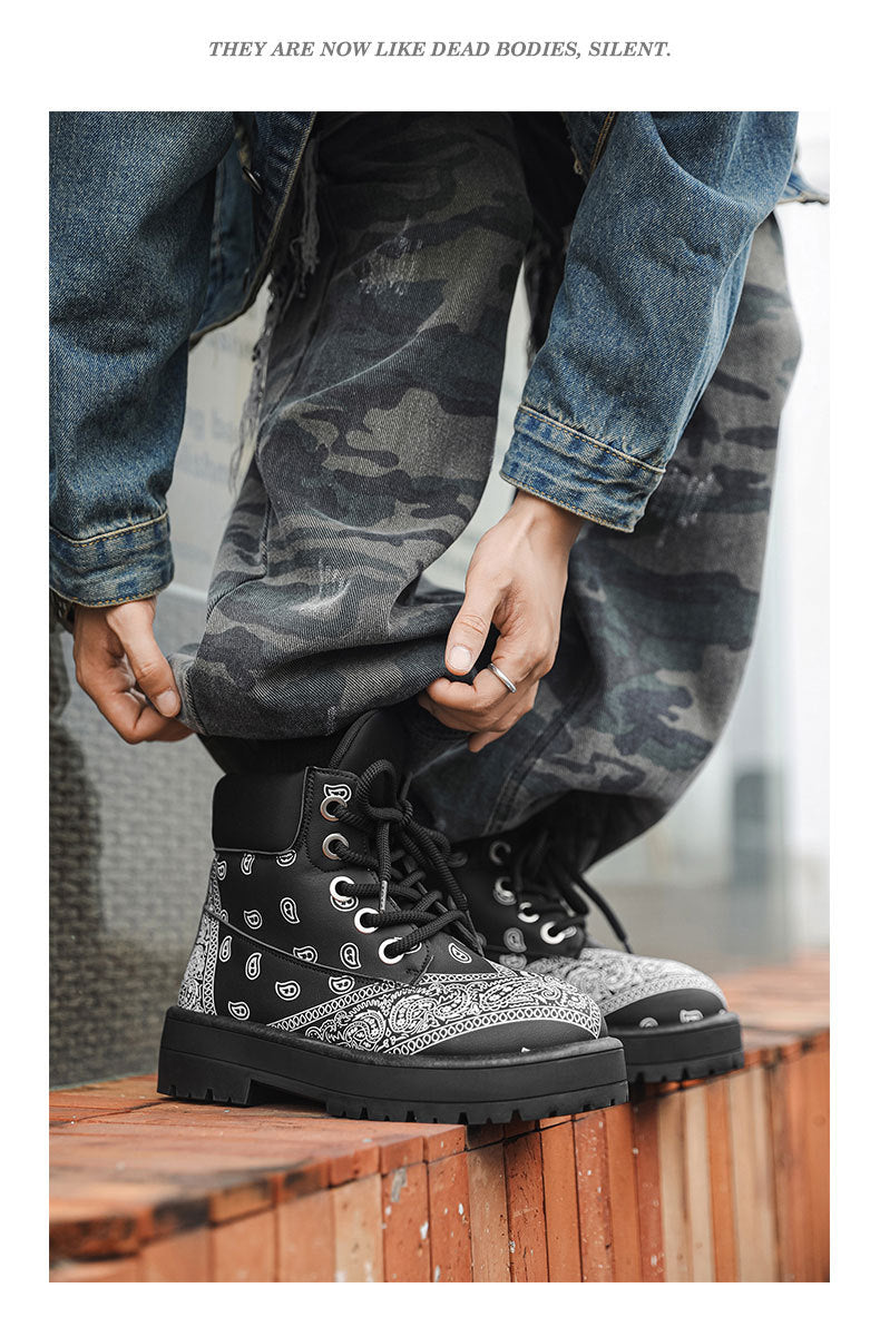 A person wearing black and white patterned lace-up boots with distressed blue denim jeans, sitting on a wooden ledge.