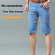 A man wearing light blue denim shorts with a brown belt and brown leather dress shoes, shown from the waist down on a light gray studio background with measurement guide lines and promotional text.