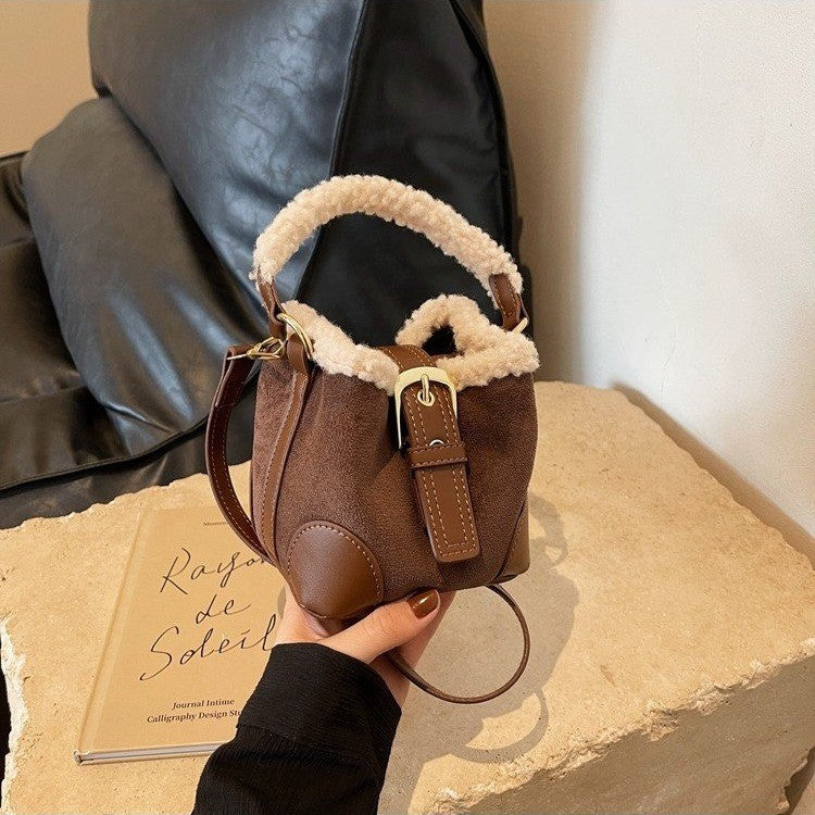 Brown leather handbag with shearling lining held by a person on a textured surface.