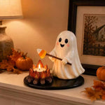 A cute white ghost figurine holding a candy corn wand, standing next to a small lit candle holder on a black base, styled on a mantel with autumn leaves, pumpkins, and a lamp.