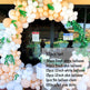 A large balloon arch decoration kit displayed in front of a glass building entrance. The arch is made of clusters of white, peach, and beige balloons with green leafy garland accents.