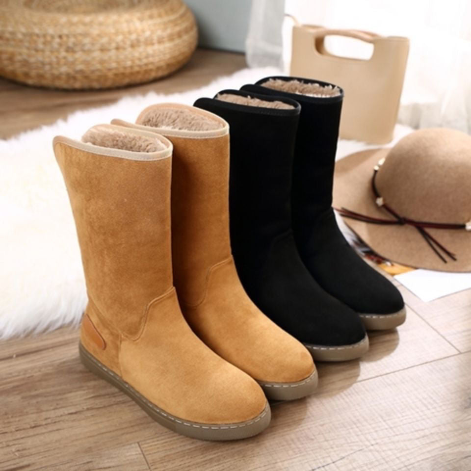 Pair of tan and black boots on a wooden floor with a hat and basket in the background.
