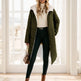 Woman wearing a green puffer coat, white turtleneck, black pants, and brown boots in a bright room.