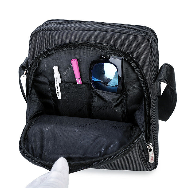 Black travel bag with compartments containing a phone, sunglasses, and other items on a white background