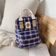 Small plaid backpack with a strawberry patch design on a bed