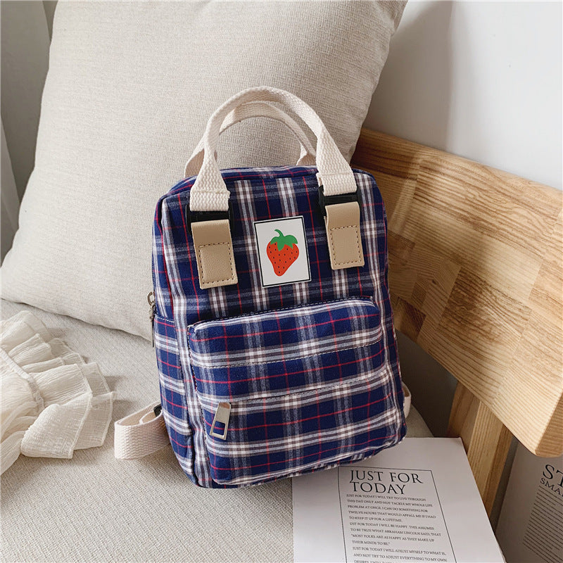 Small plaid backpack with a strawberry patch design on a bed