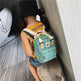 Person wearing a green plaid backpack with a heart emblem on a wooden floor.
