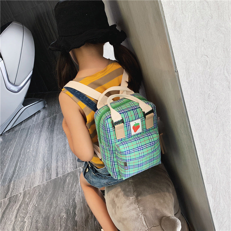 Person wearing a green plaid backpack with a heart emblem on a wooden floor.
