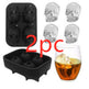 Two black skull-shaped ice cube trays with a glass of whiskey and ice cubes.