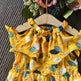 Yellow floral dress on a hanger against a textured brown background