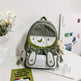 Green and white backpack with bunny ears on a table with flowers and papers.