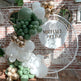 Balloon arch with green, white, and gold balloons against a brick wall with 'Michael & Elise' sign.