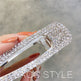Sparkling silver barrette held by a hand with orange nail polish on a blurred background.