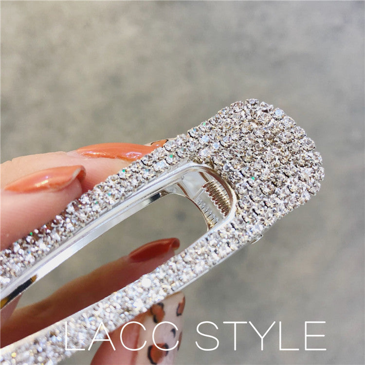 Sparkling silver barrette held by a hand with orange nail polish on a blurred background.