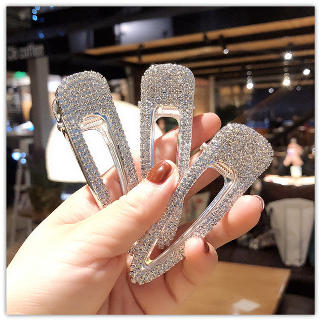 Three sparkling hair clips held by a hand in an indoor setting.