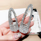 Shiny silver shoe-shaped earrings held in a hand with a blurred background
