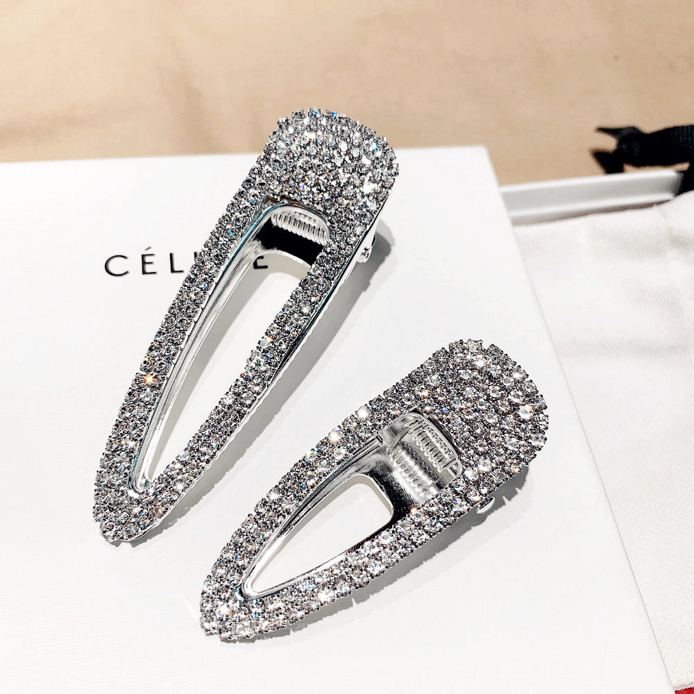 Two silver hair clips with clear gemstones on a white surface with 'Celine' branding.