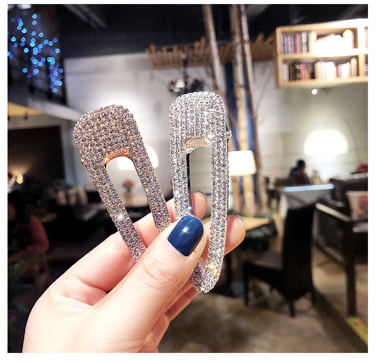 Hand holding two sparkling hair clips with a blurred indoor background