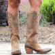 Brown cowboy boots worn by a person with a blurred natural background