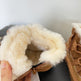 Close-up of brown winter boots with fluffy white lining held by a hand against a light background.