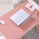 Pink desk with laptop, mouse, and stationery on a wooden floor.
