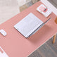 Pink desk with laptop, mouse, and stationery on a wooden floor.