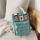 Green plaid bag with a strawberry patch design on a bed